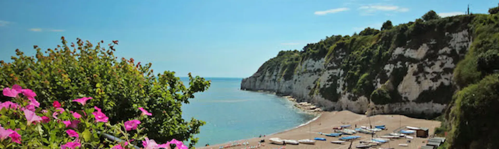  A large shingle East Devon beach in a cove surrounded by tall cliffs. Small fishing boats lie on the beach.