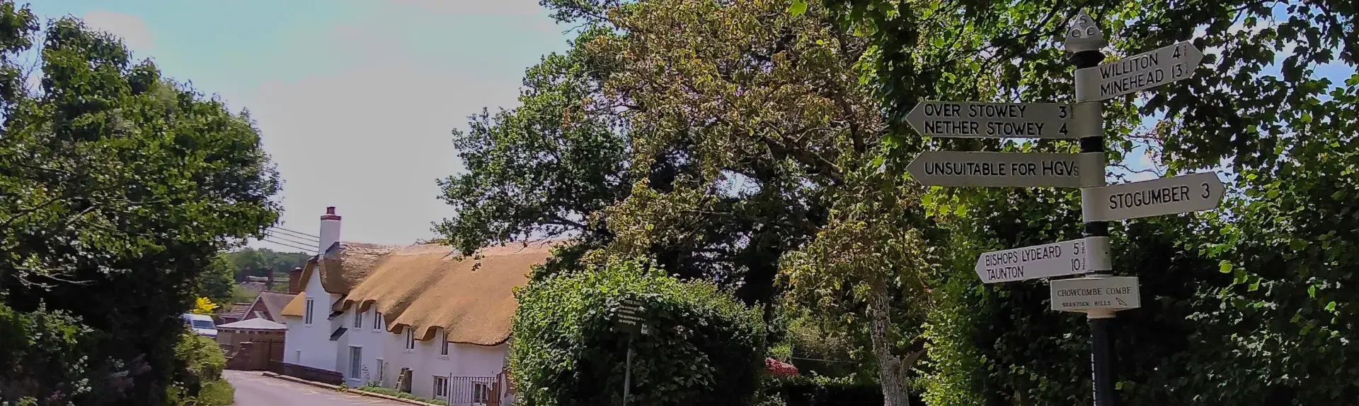 A quiet village lane lined by trees and a row of thatched cottages in The Quantock Hills