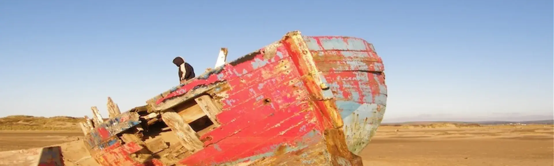 An old, weather-beaten boat abandoned on a sandy beach in North Devon