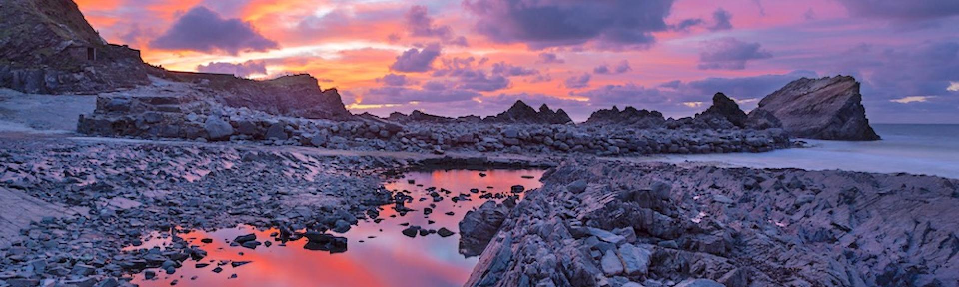 A sunset over a rocky beach with large rock pools reflecting the clouds.