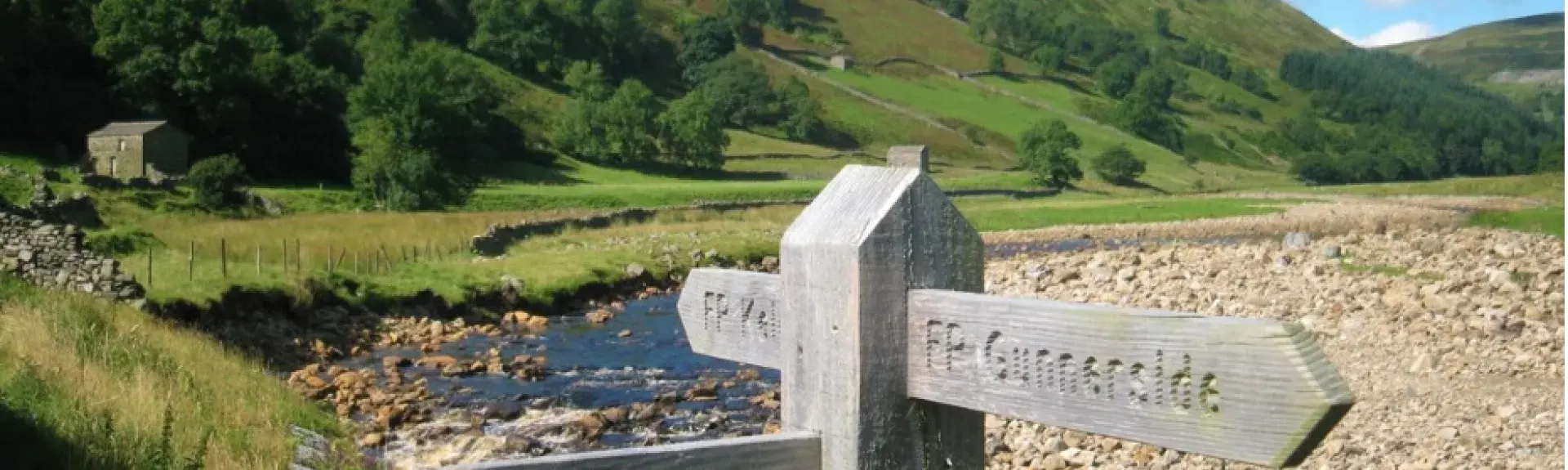 A wooden finger post for footpaths alongside a shallow river.