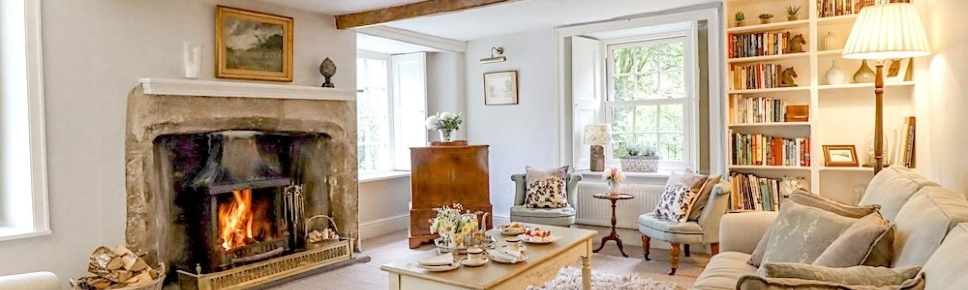 A luxurious farm cottage lounge with oak beams sofas inglenook fireplace.