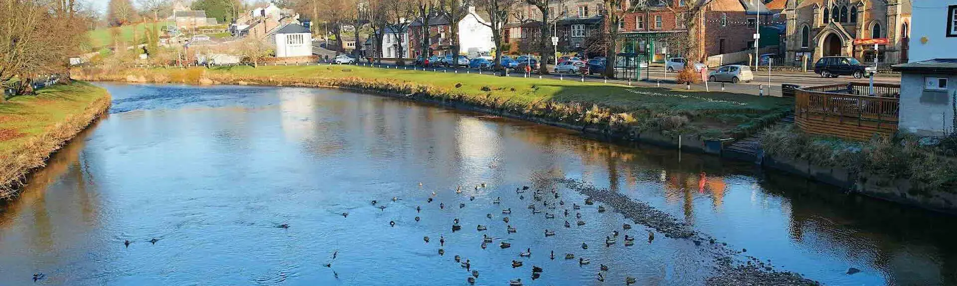 Town houses and shops overlook a wide, shallow river bordered by trees in winter.