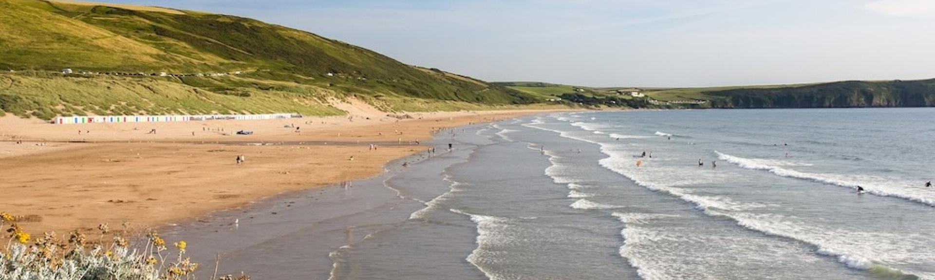 Surfing waves roll in to a long sandy beach backed by sand dunes.