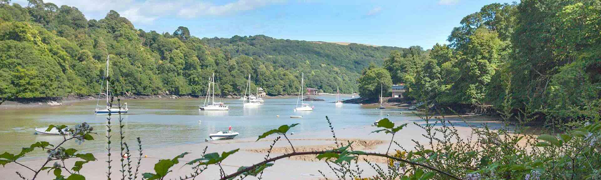 Small boats moored on a sandy river creek lined by mature woods at low tide,