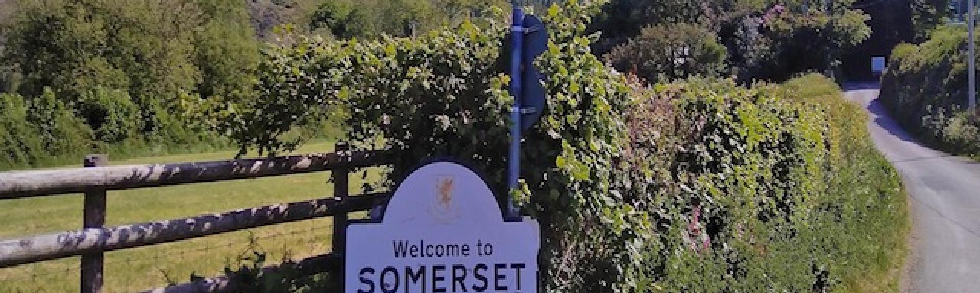 A ‘Welcome to Somerset’ road sign stands on a winding country lane that curls into the distance.