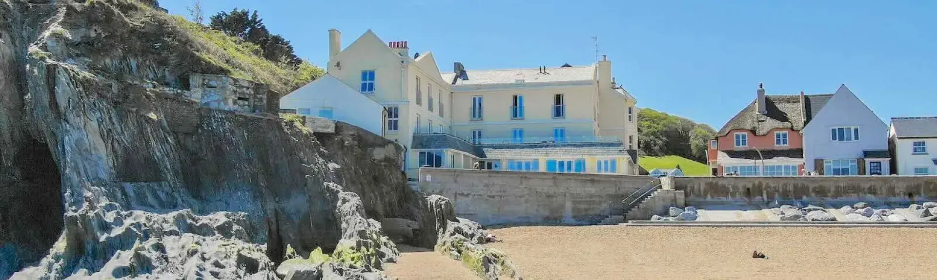 A 2-storey apartment building overlooks a clear sea with tiny waves breaking on a sandy beach.