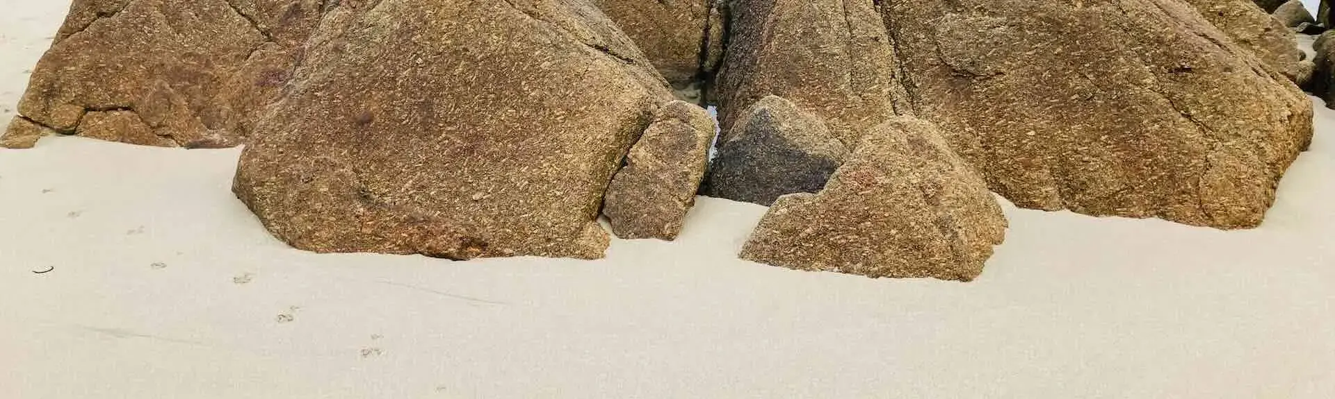 Cornish granite rocks embedded in sand on a beach at low tide.