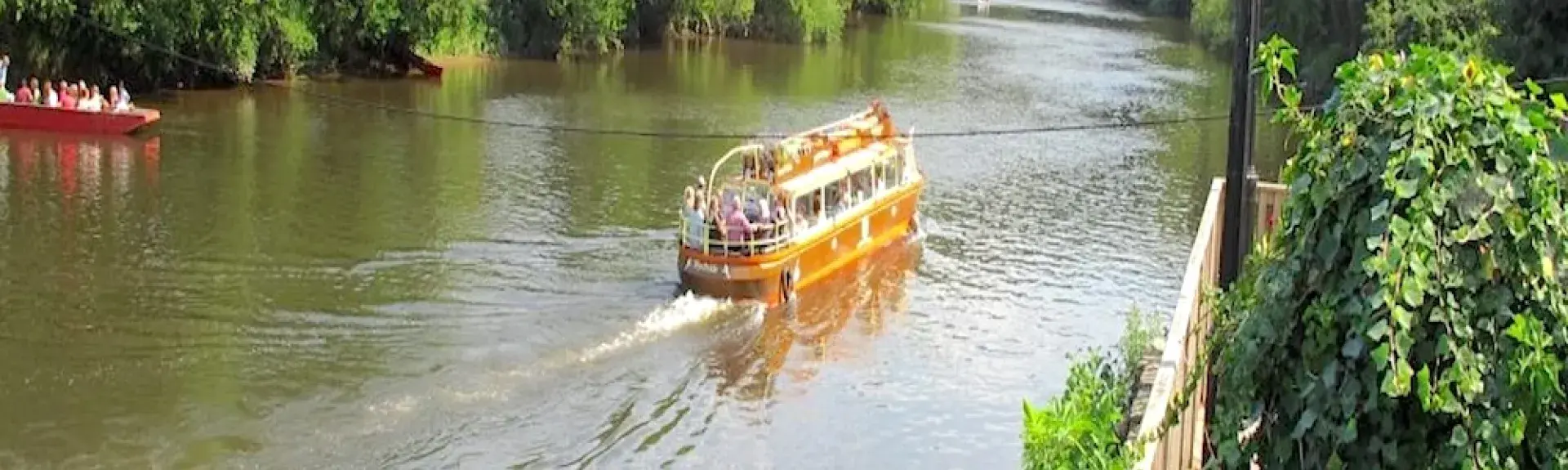 A small cruise boat makes its way upstream around a tree-lined River Wye.