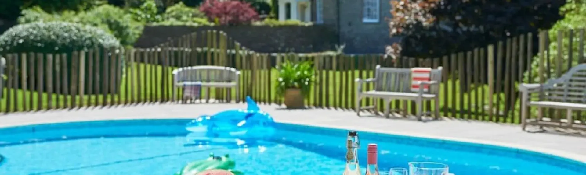 A lunch table on a terrace overlooking an outdoor pool overlooked by a granite house on Dartmoor.