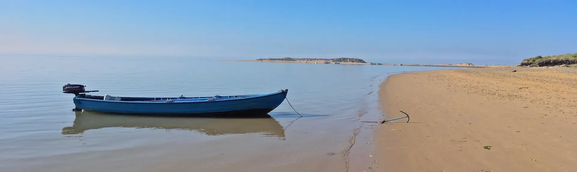 A rowing boat anchored at the waters edge on a long sandy beach in North Devon.