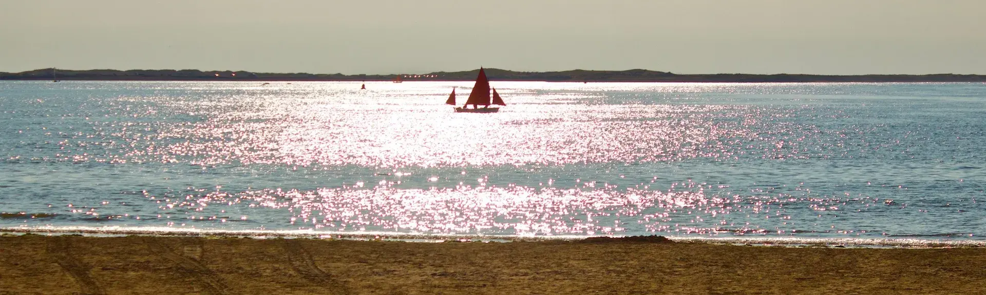 A sailing boat silhouetted against sunlit waves off Instow Beach in North Devon 