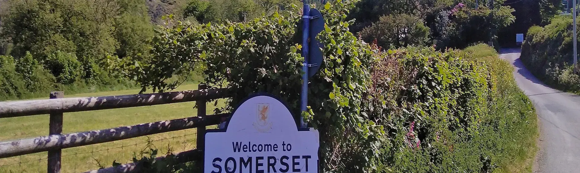 A 'Welcome to Somerset' sign on a quiet, winding country lane.