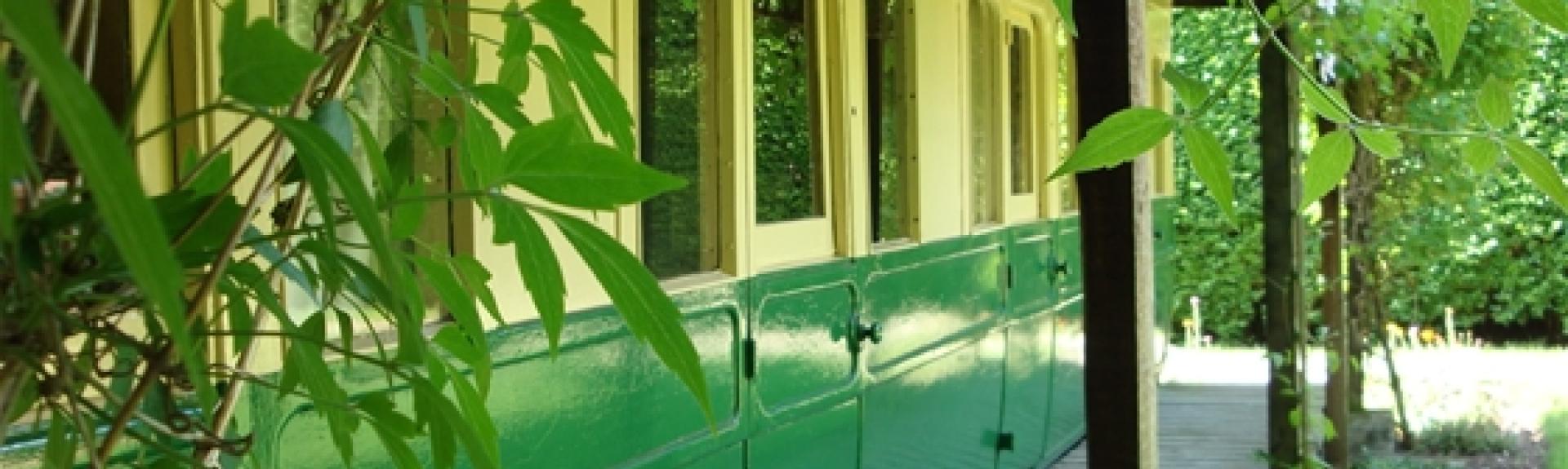 The exterior of restored railway carriage converted into self-ctering holiday accommodation with a vine-covered sun deck.