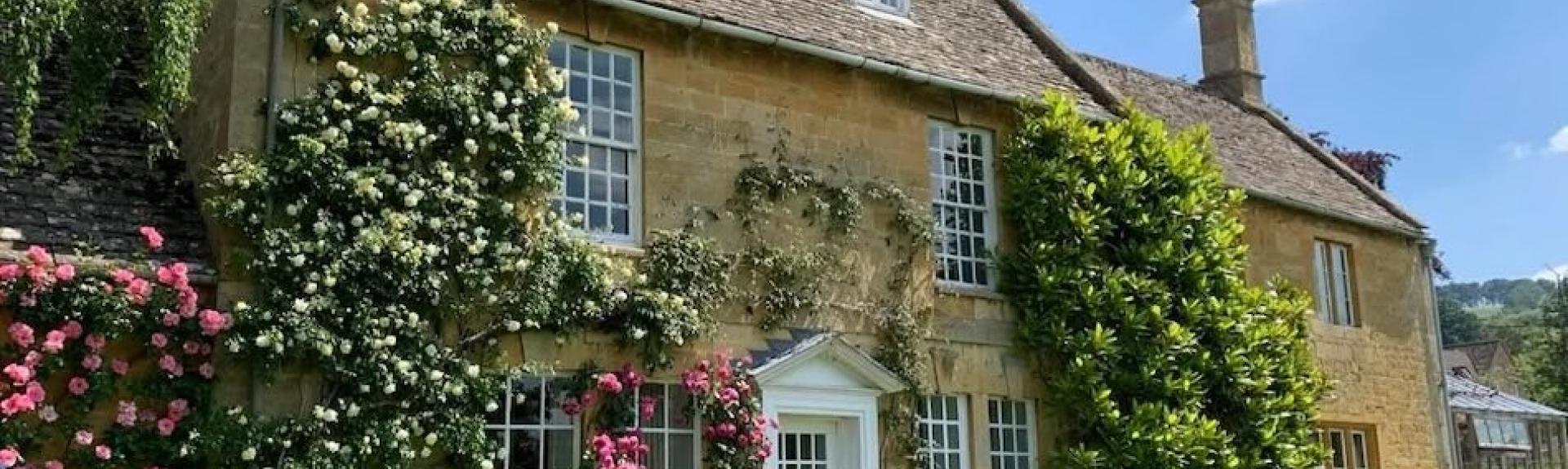 A stone-built house with roses and wisteria climbing the walls.