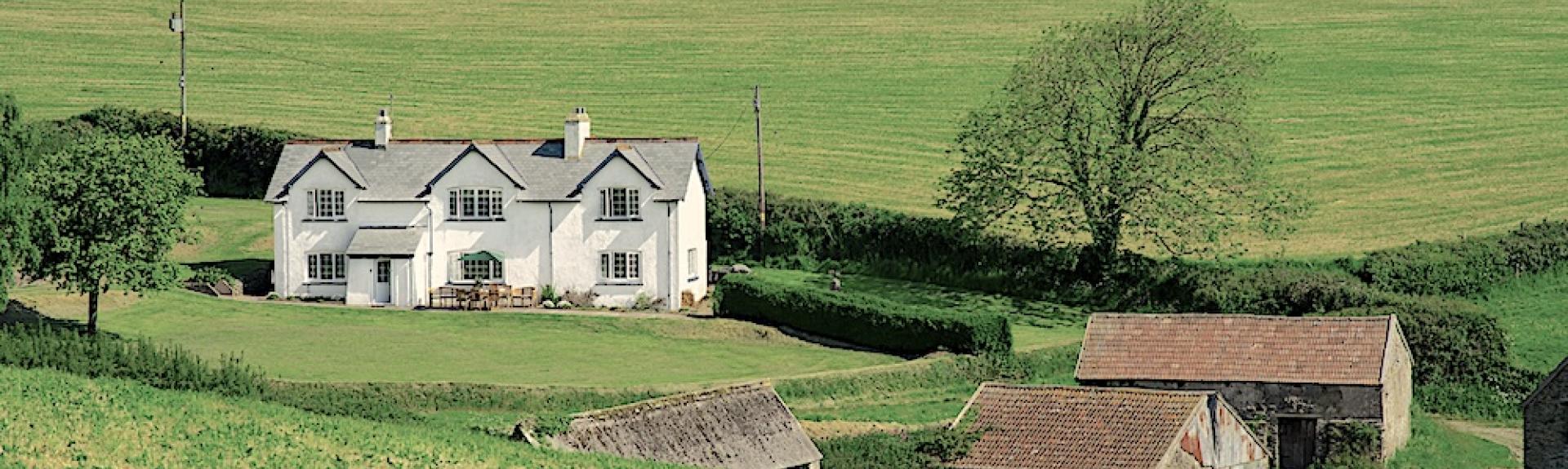 A large North Devon farmhouse with a cluster of three barns, all surrounded by green fields.