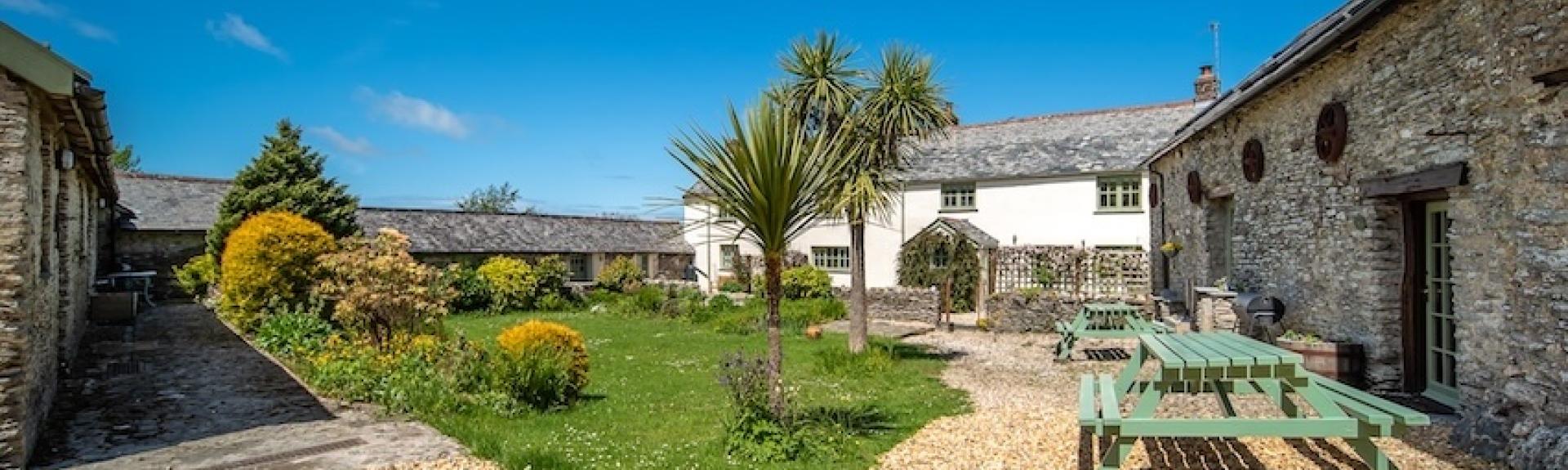 A large Devon farmhouse overlooks a lawn and drive with a picnic table.