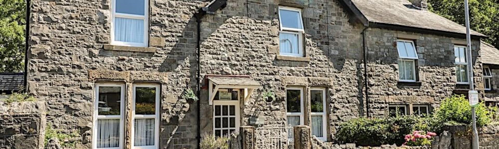 Stone-built Cumbrian holiday cottage with a front garden behind a low stone wall.