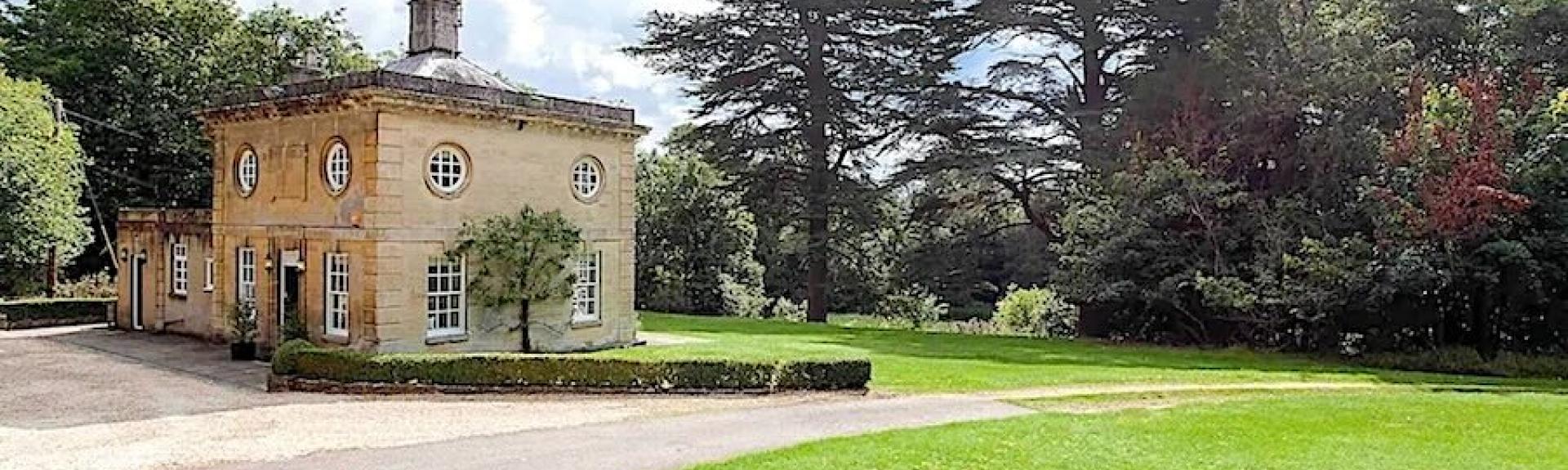 Exterior of a stone-built Cotswold country house surrounded by trees and parkland.