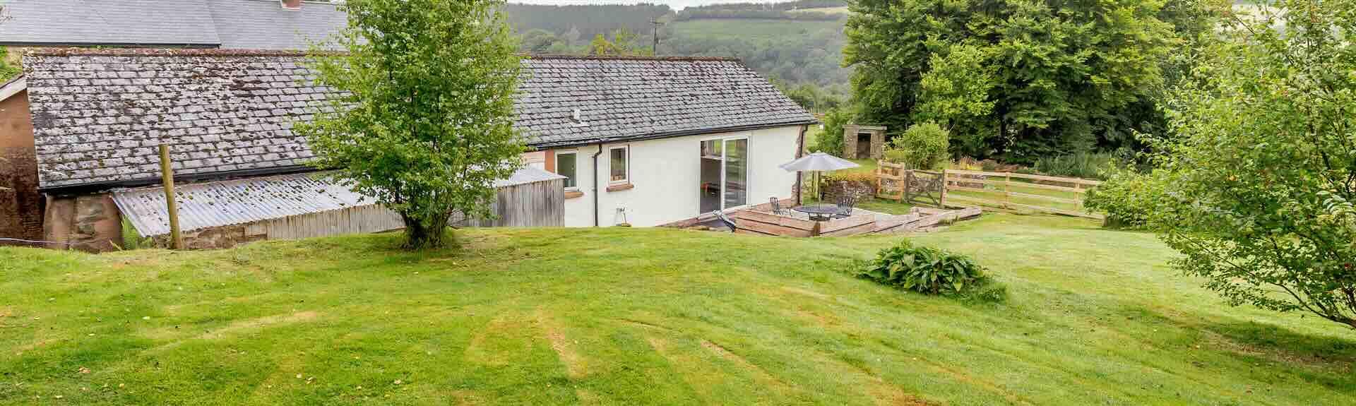 A large lawn slopes down to a large bungalow with Exmoor views beyond.