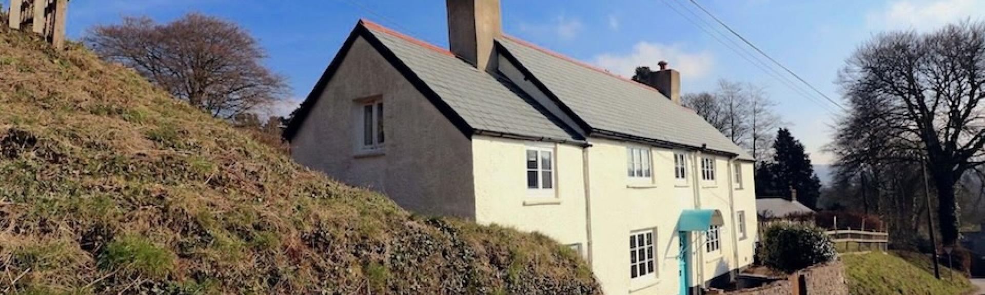 An Exmoor Longhouse overlooks a quiet, steep-banked country lane.