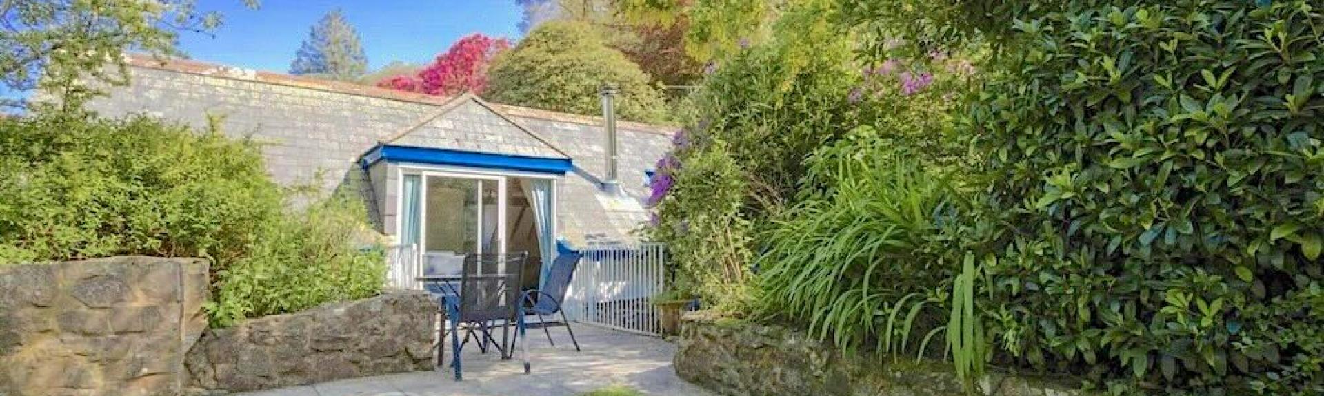   A footpath between a lawn and mature shrubs leads to a stone-built rural cottage.