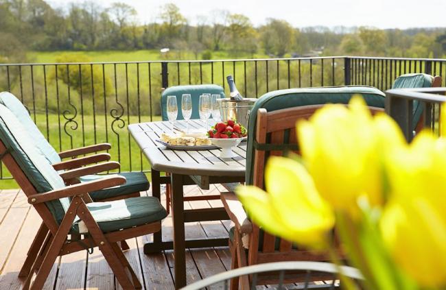 A dining table and chairs on a deck of a Wiltshire holiday cottage with fields in the background.