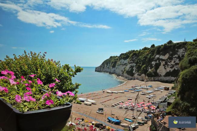 Beer's shingle beach on which small fishing boats and cafe tables are laid out nestles beneath steep, vegetation-covered chalk cliffs