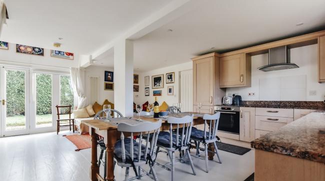 An open plan kitchen area with dining table, fitted kitchen units, a lounge with sofas and French Windows to the garden.