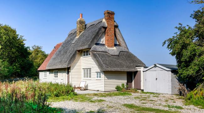 A slate roofed, clapperboard essex cottage with tall brick chimney stacks.