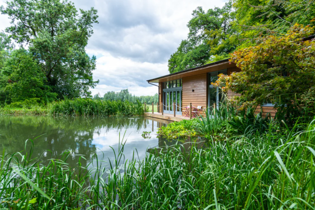 A wooden holiday lodge looks out across a reed-fringed river in Hampshire