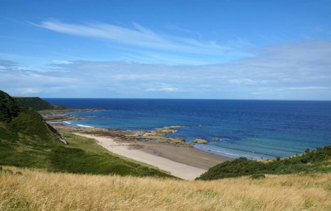 View of low grassy hills sloping down to a small beach in Banff, Aberdeenshire