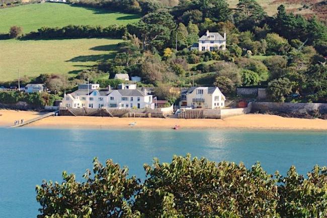 An estuary view at high tide of a beach with a handful of houses above it.