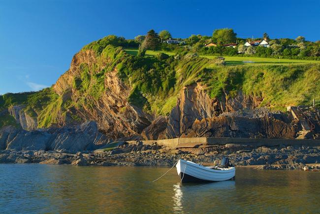 Arrow-boat anchored off a rocky shore beneath steep cliffs in Combe Martin.