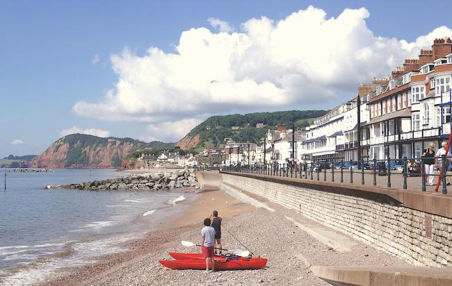 An esplanade lined by cafes and hotels overlooks a shingle beach in East Devon.