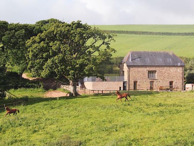 A remote South Devon barn conversion surrounded by hilly open fields in summer.