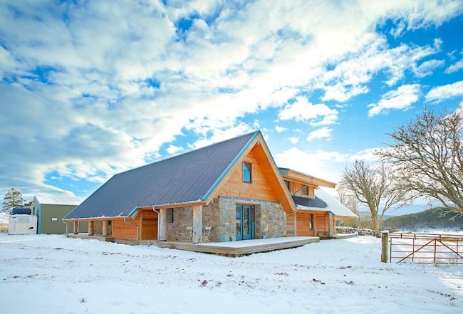 A wooden pine holiday lodge in the snow against a backdrop of a clouded sky.