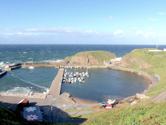 Aerial view of a Scottish harbour with small fishing boats in a natural cove.