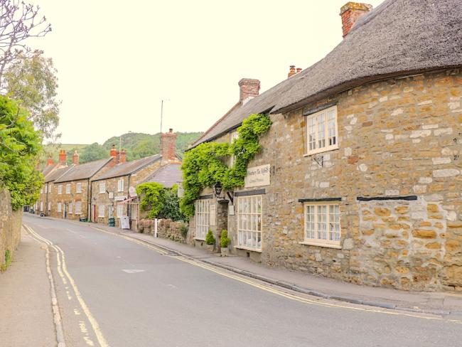 A villge street in Dorset lined by old ston-bult cottages with thatched roofs.