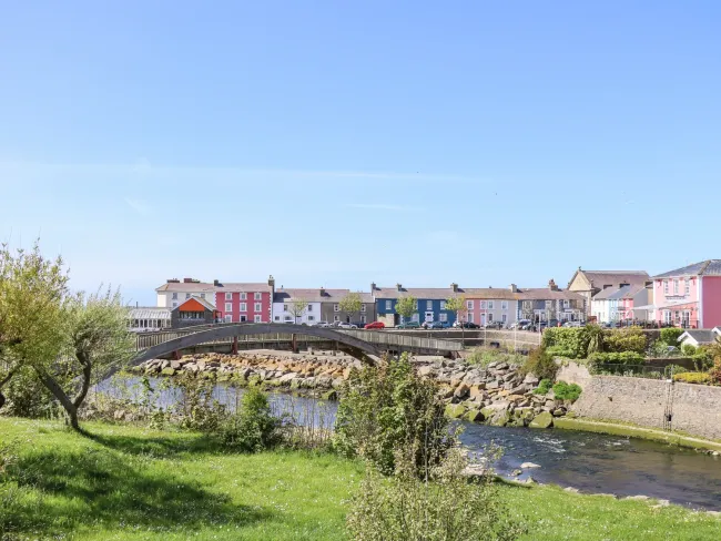 A graceful arched bridge spans a river with rocky banks flowing thrioughg Aberaeron