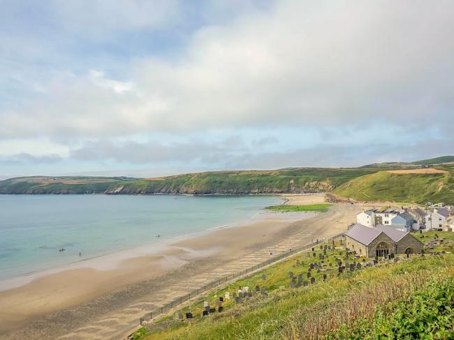 A Welsh beach stretches around a wide bay backed by low hills.