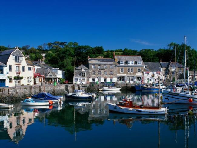 Fishing boats and small craft moored in Padstow harbour overlooked by shops and houses.