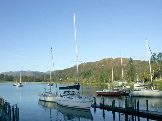 Pleasure boats moored  to a jetty on the calm surface of a lake in Ambleside.