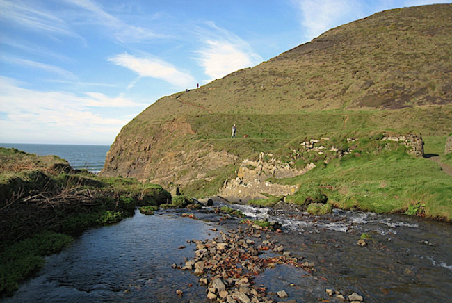 A small river in a valley flows through walks towards the distant sea