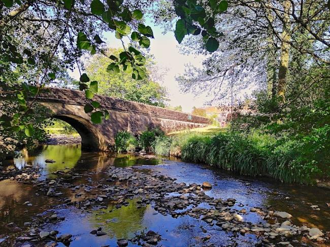 An ancient stone bridge arches across a wide shallow river.