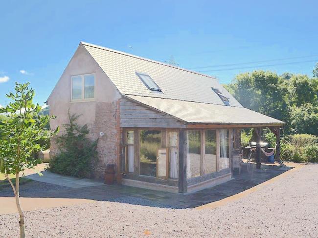 A stone country cottage with a large sun room and a hammock on its deck.