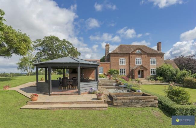 A large detached house overlooks a garden with lawns and a hexagonal summerhouse.