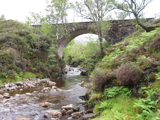 A high stone arched bridge spans a mountain stream.