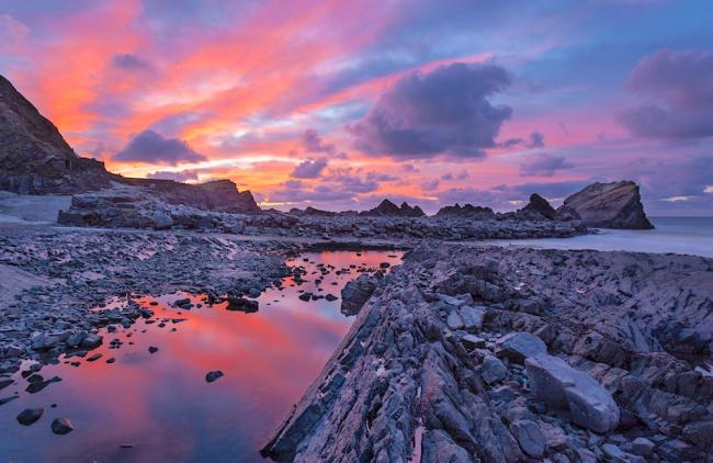 A sunset over a rocky beach with large rock pools reflecting the clouds.