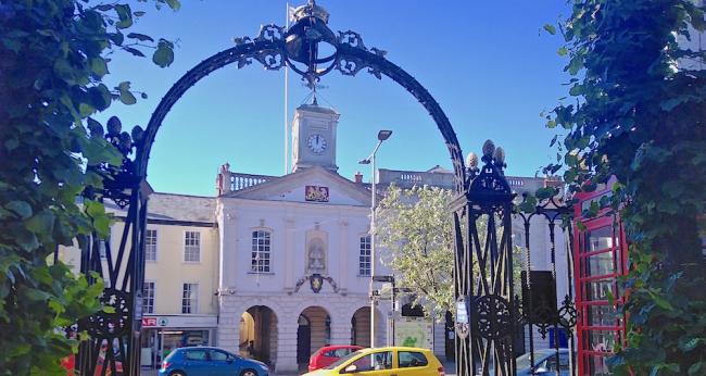 A town hall with a clock tower seen  through an ornate ironwork arch